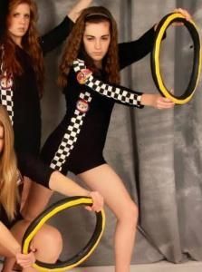 Two performers in black outfits pose with yellow rings against a gray curtain.