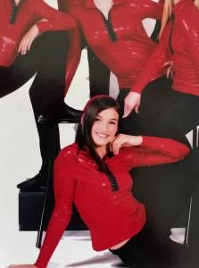 Group of people in red outfits posing against a black-and-white studio backdrop, one seated smiling in front