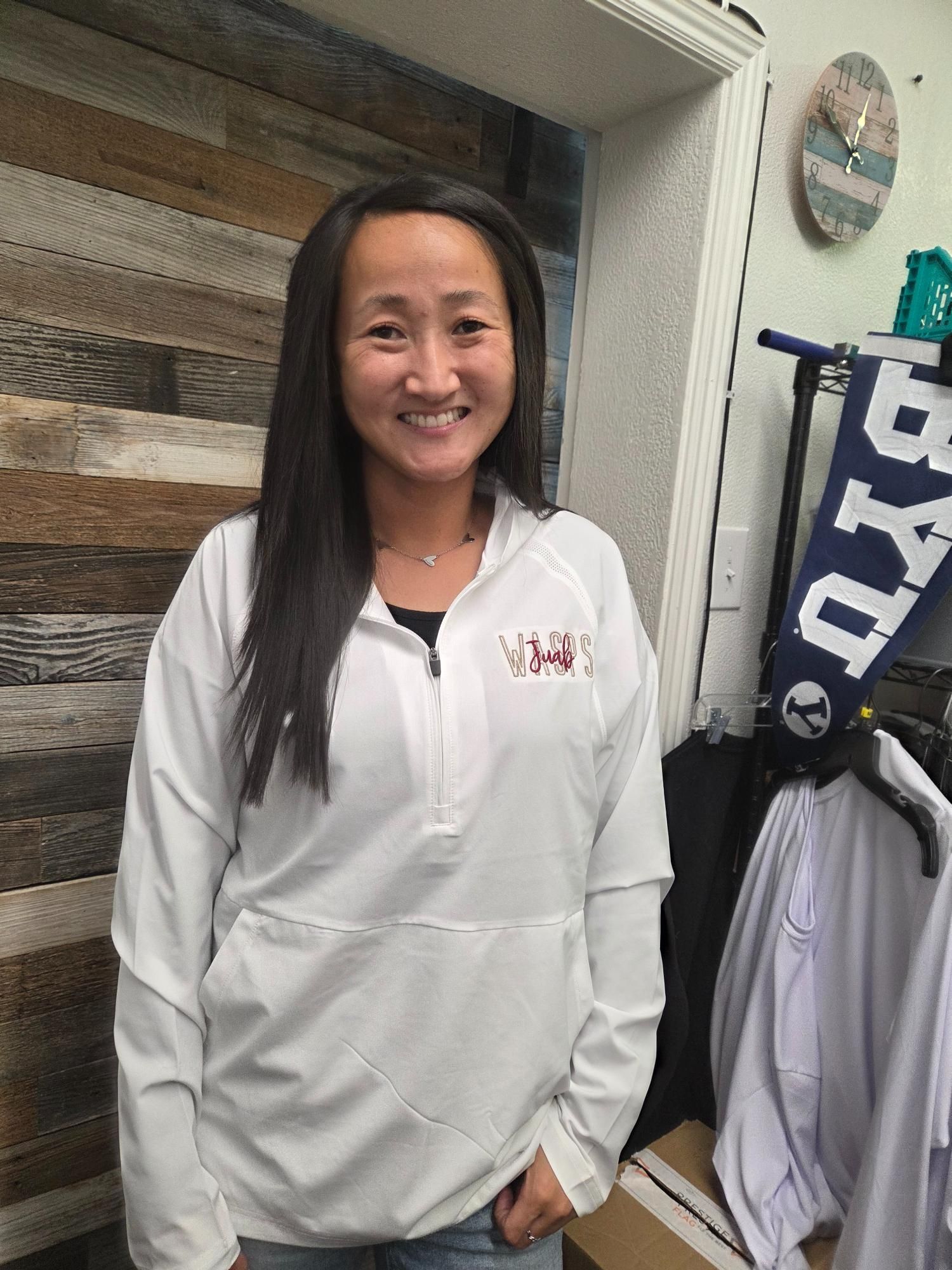 Woman in white jacket smiles inside a store, with BYU flag visible.