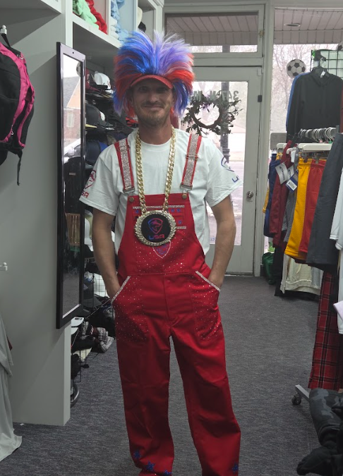 Person in red overalls and colorful wig standing in a clothing store aisle.
