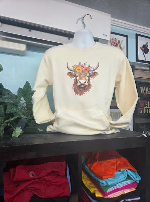 Cream sweatshirt with a colorful cow design displayed on a store shelf.