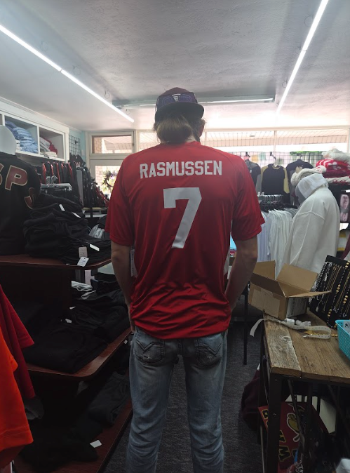 Man wearing a red Rasmussen jersey with number 7 in a crowded store aisle