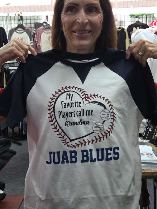 Woman holding up a white and black T-shirt with a baseball heart logo and the words “JUAB BLUES.”