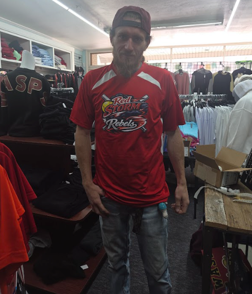 Man in red sports jersey and backward cap standing in a clothing store aisle.