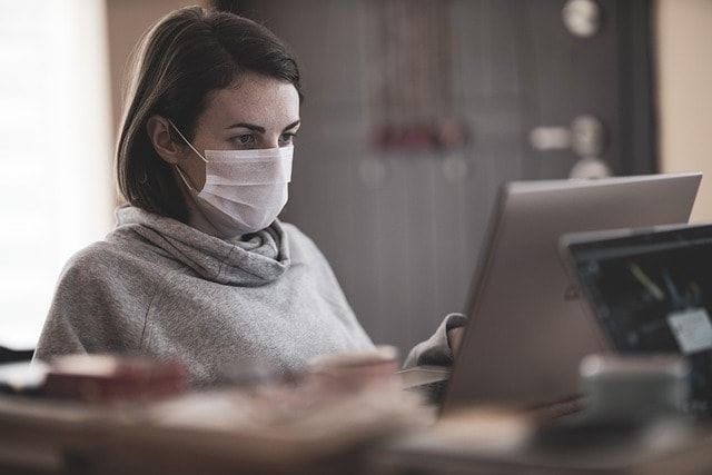 A woman wearing a face mask is using a laptop computer.