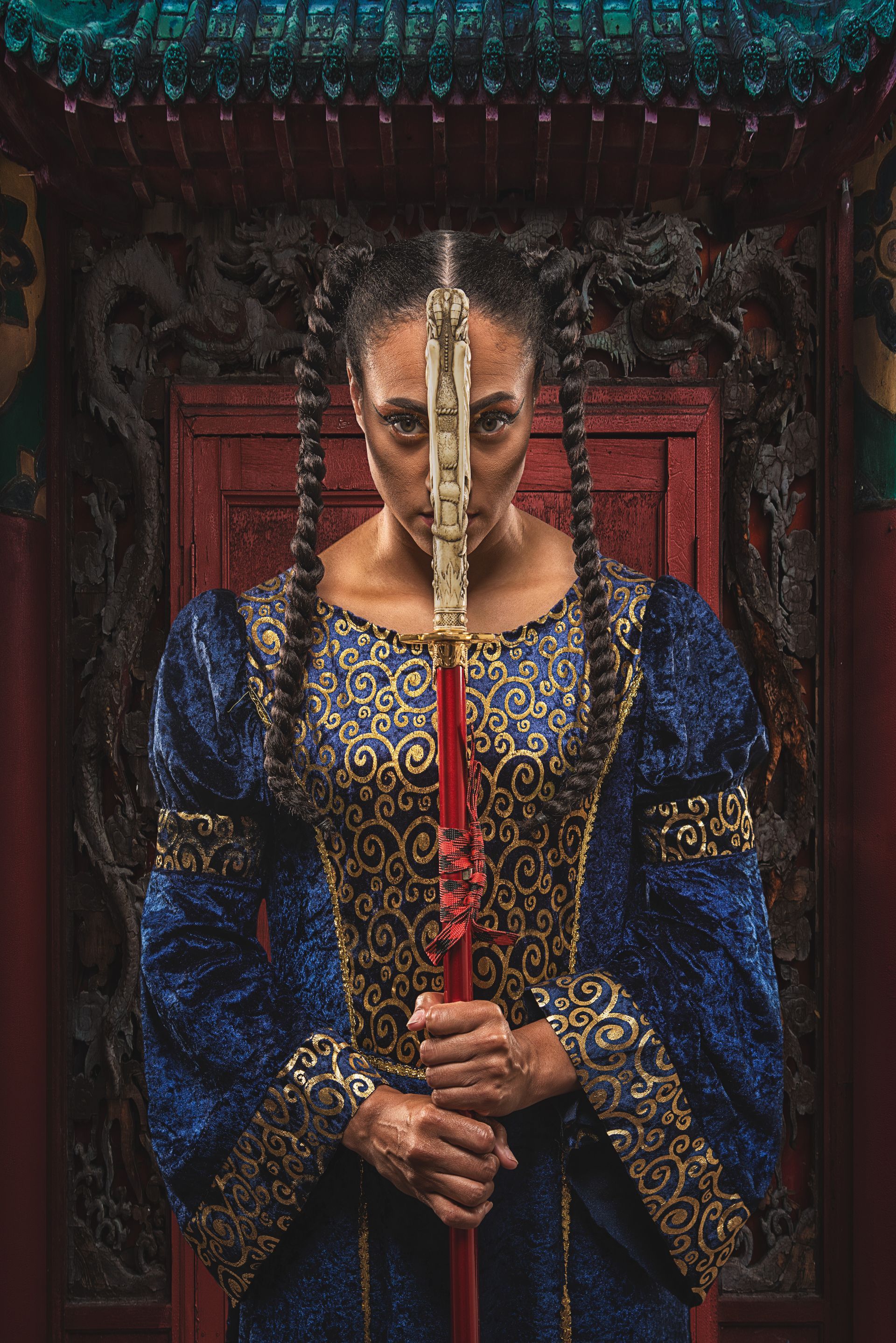 Woman holding a sword, obscured face. Wearing a blue and gold embellished dress, in an Asian-style setting.
