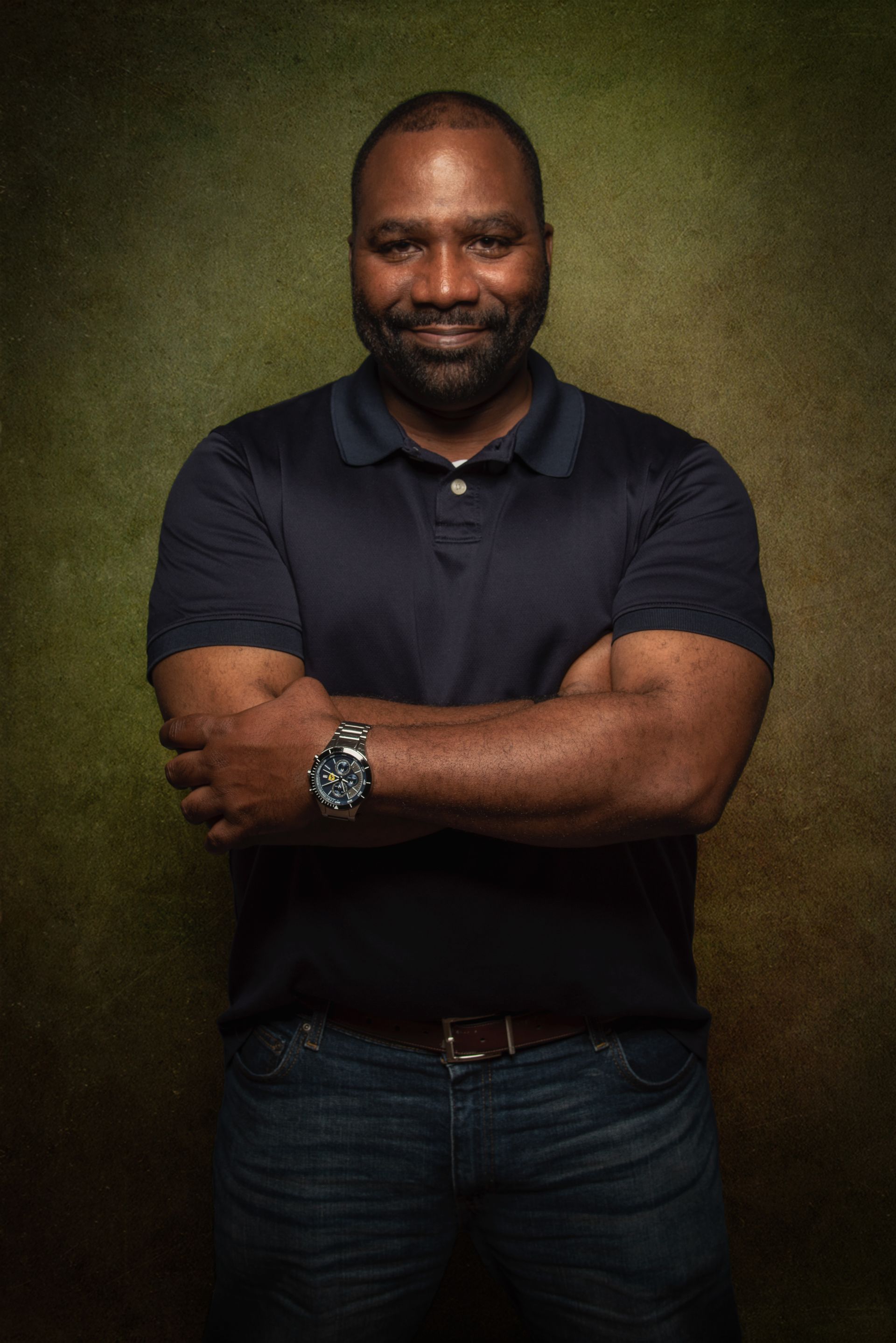 Man in dark blue shirt and jeans, arms crossed, smiling.