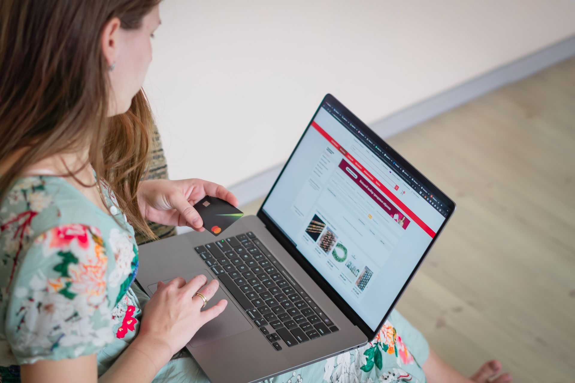 Woman using a laptop on a floor, browsing a website with a red header.