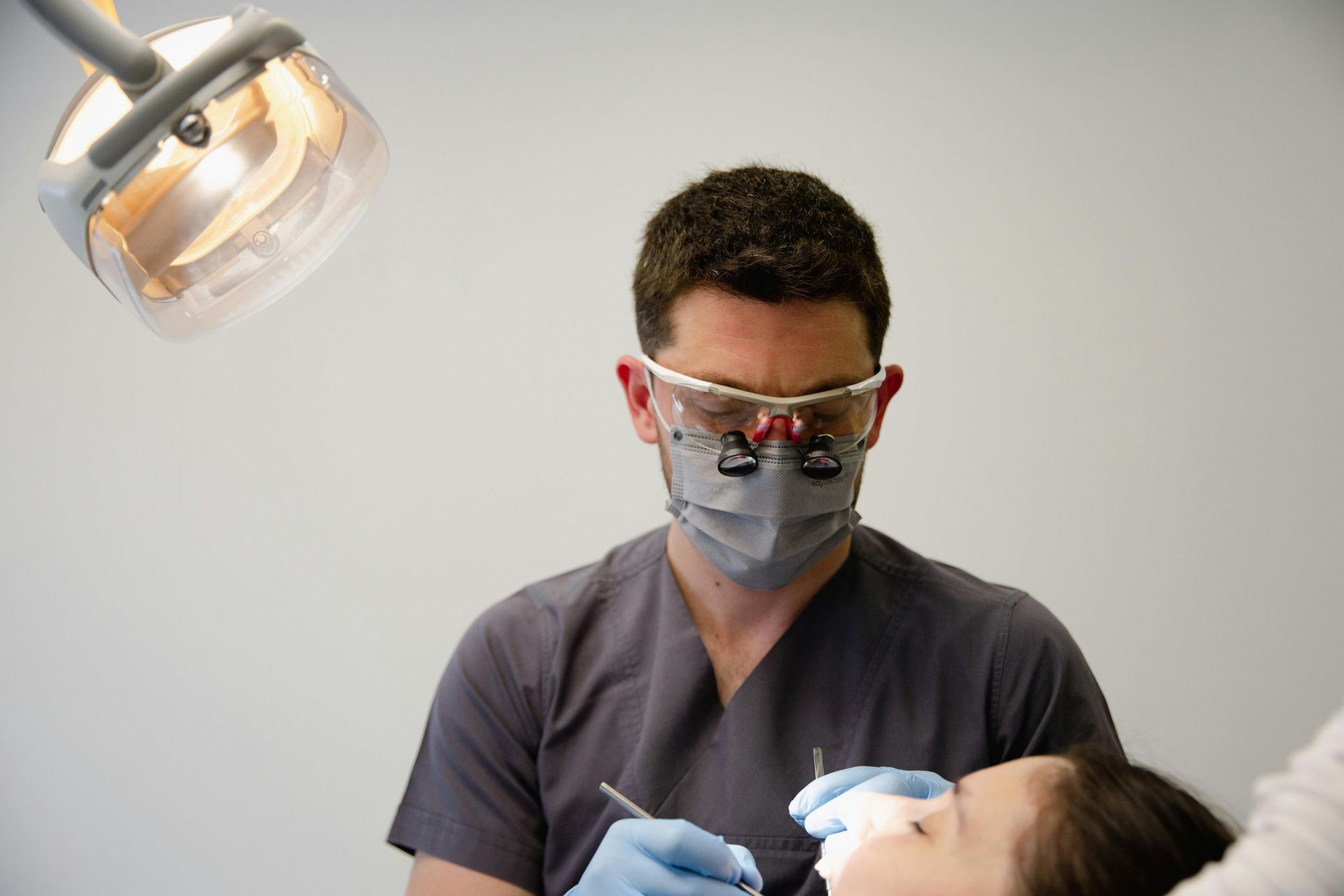 A dentist wearing a mask and glasses examines a patient 's teeth