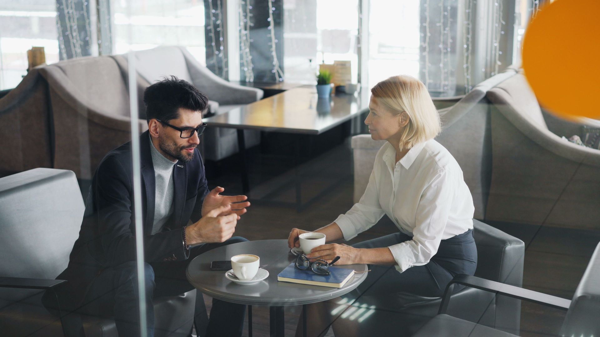 Two people talking over coffee at a small table in a modern lounge.