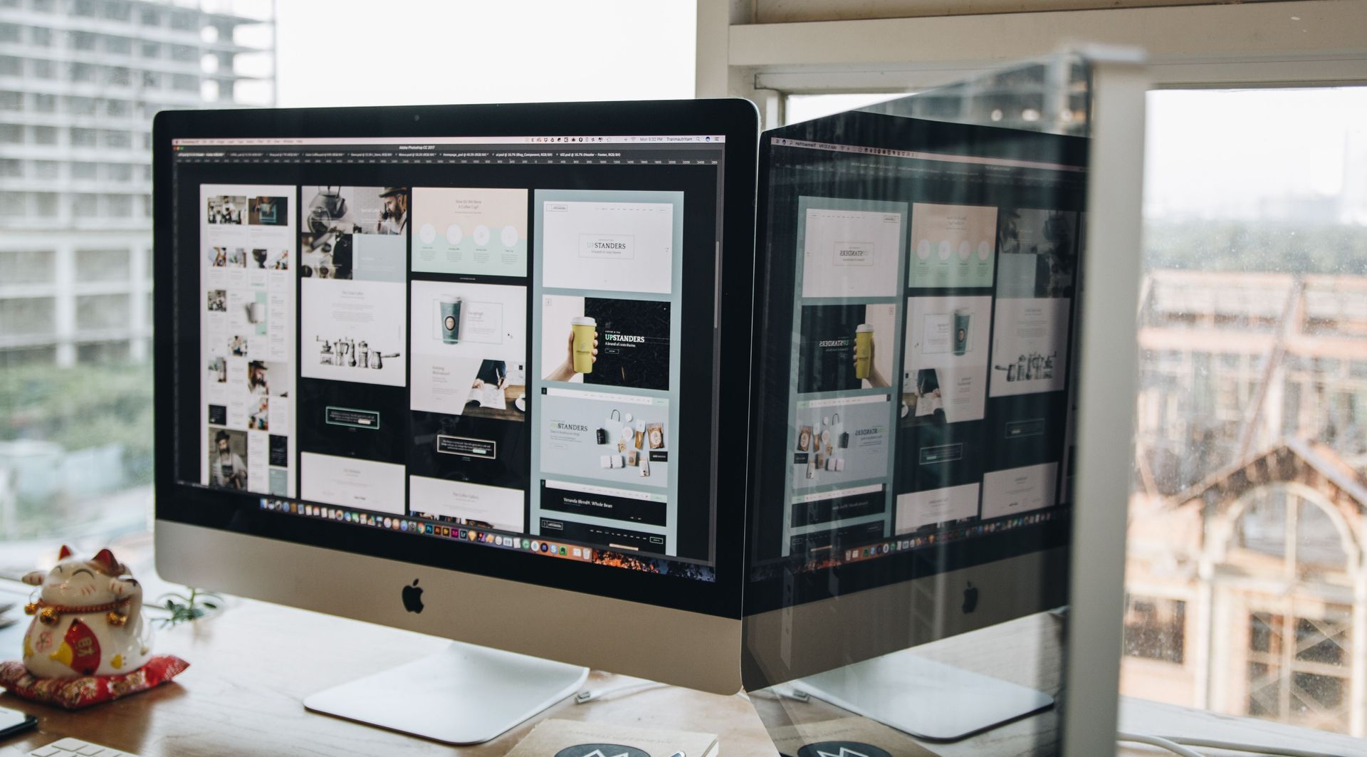 Dual monitors on a desk displaying a design mood board in a bright office by a window