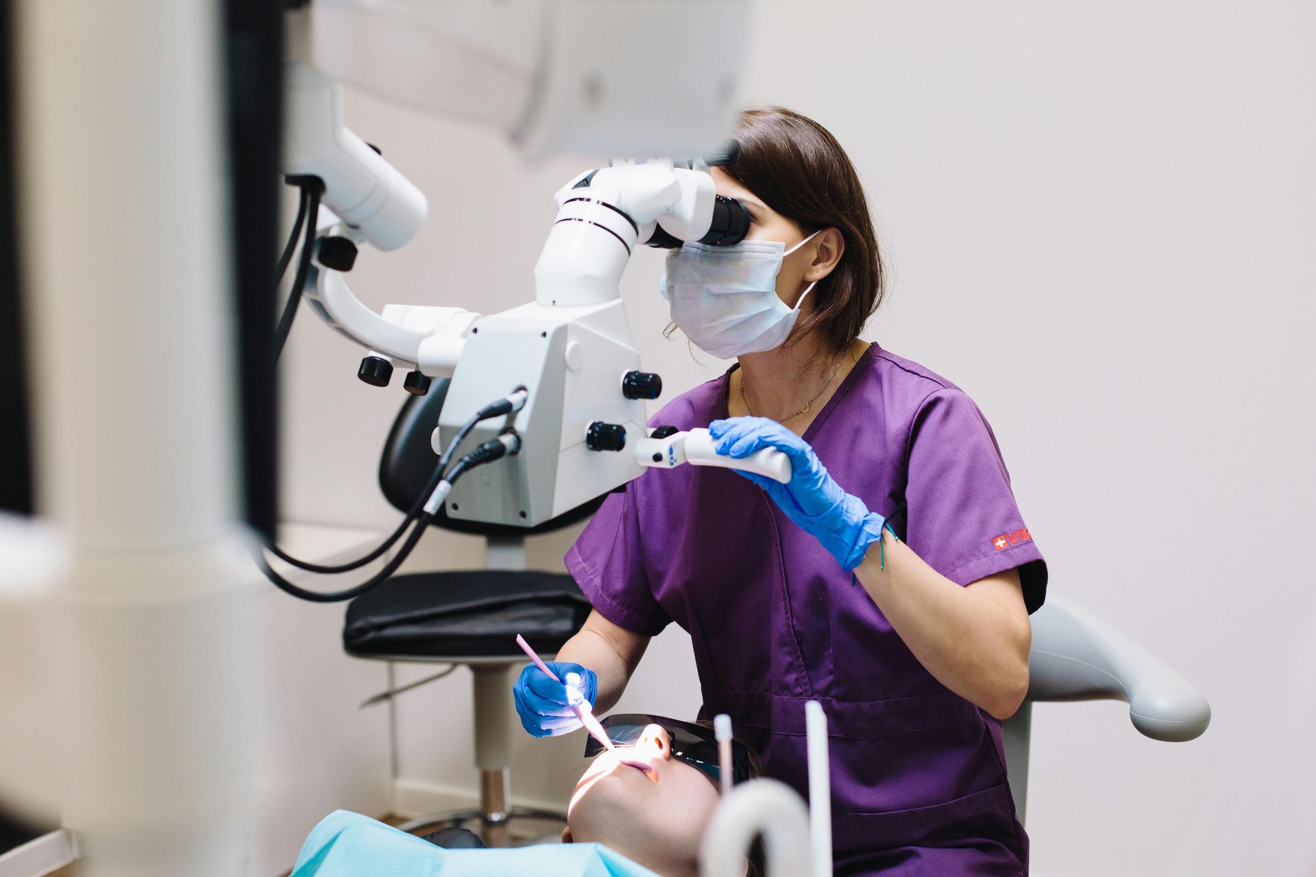A female dentist is examining a patient 's teeth under a microscope.