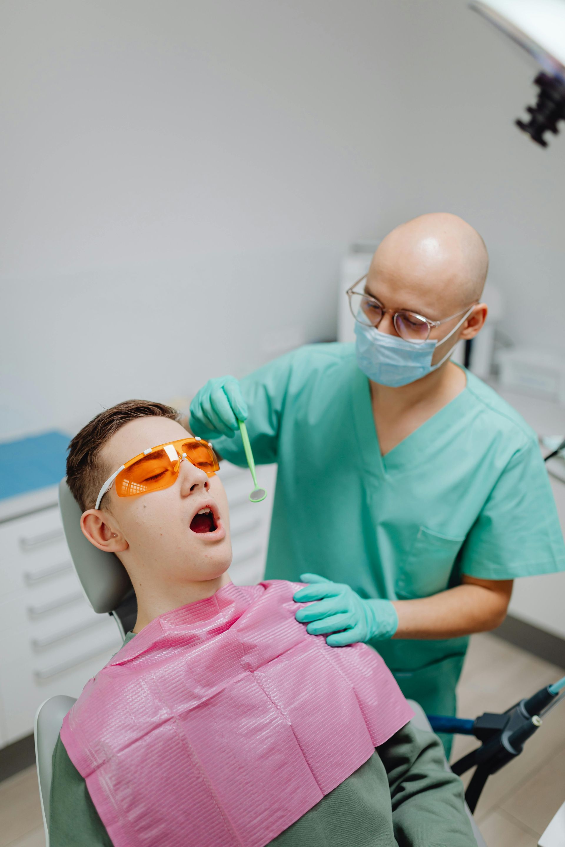 A man is sitting in a dental chair while a dentist examines his teeth.