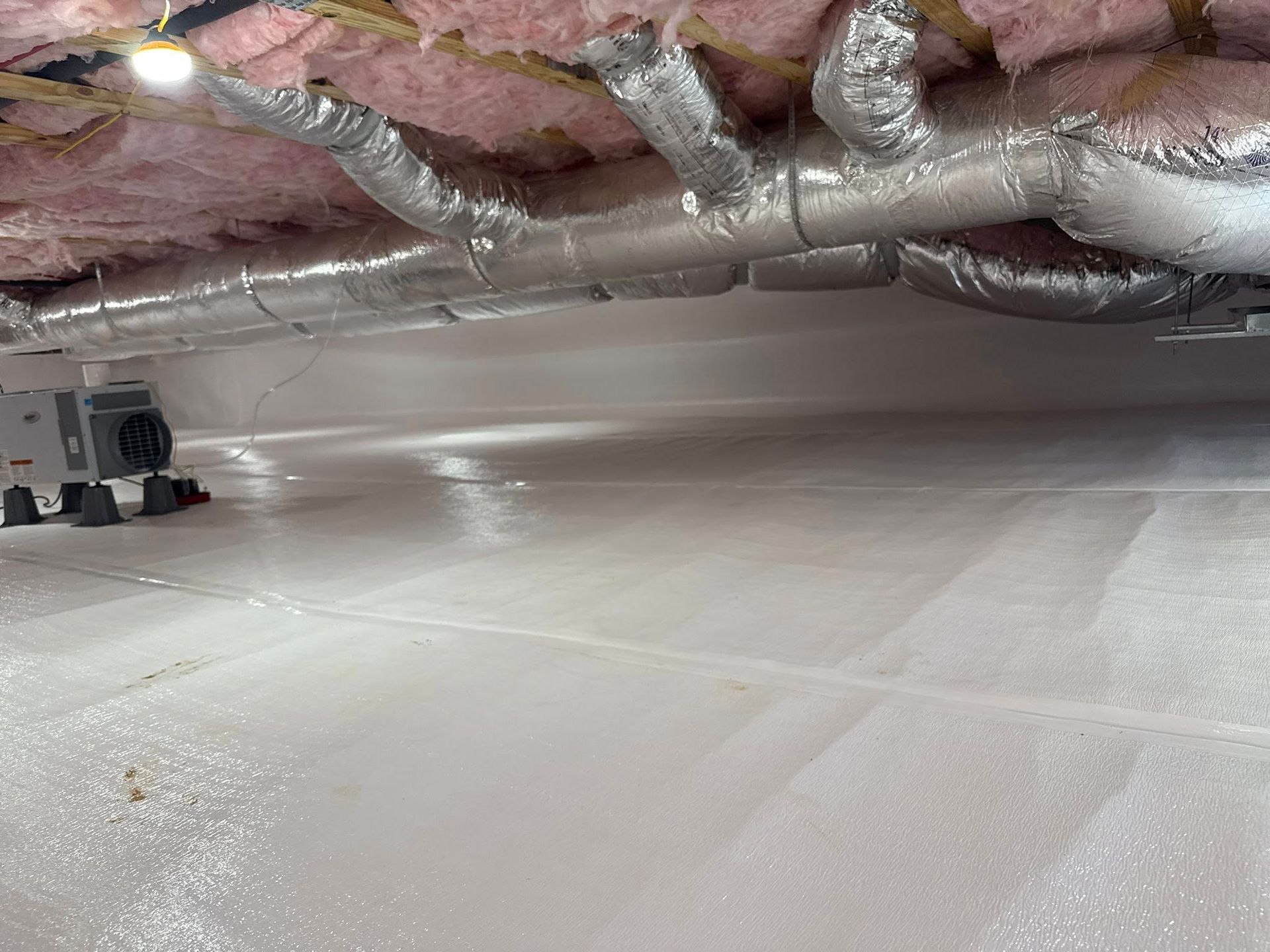 Crawl space with white vapor barrier, insulation, ductwork, and an air handler.