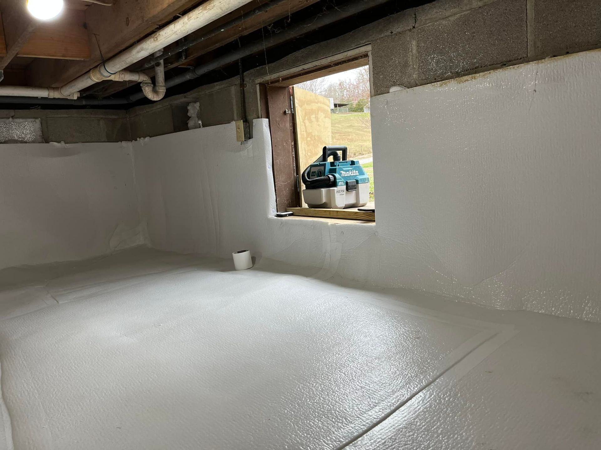 Basement interior with white coating on walls and floor, window, and tools.