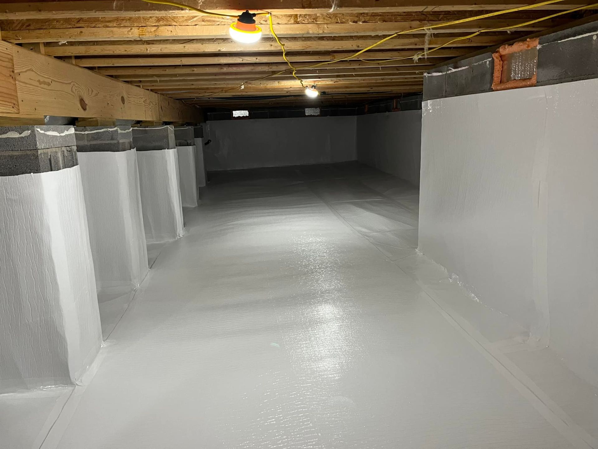 Clean white crawl space with support beams, concrete pillars, and painted walls.