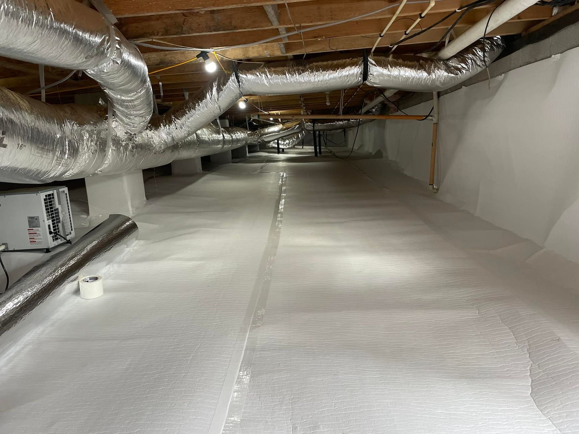 Crawl space with white vapor barrier flooring and ductwork.