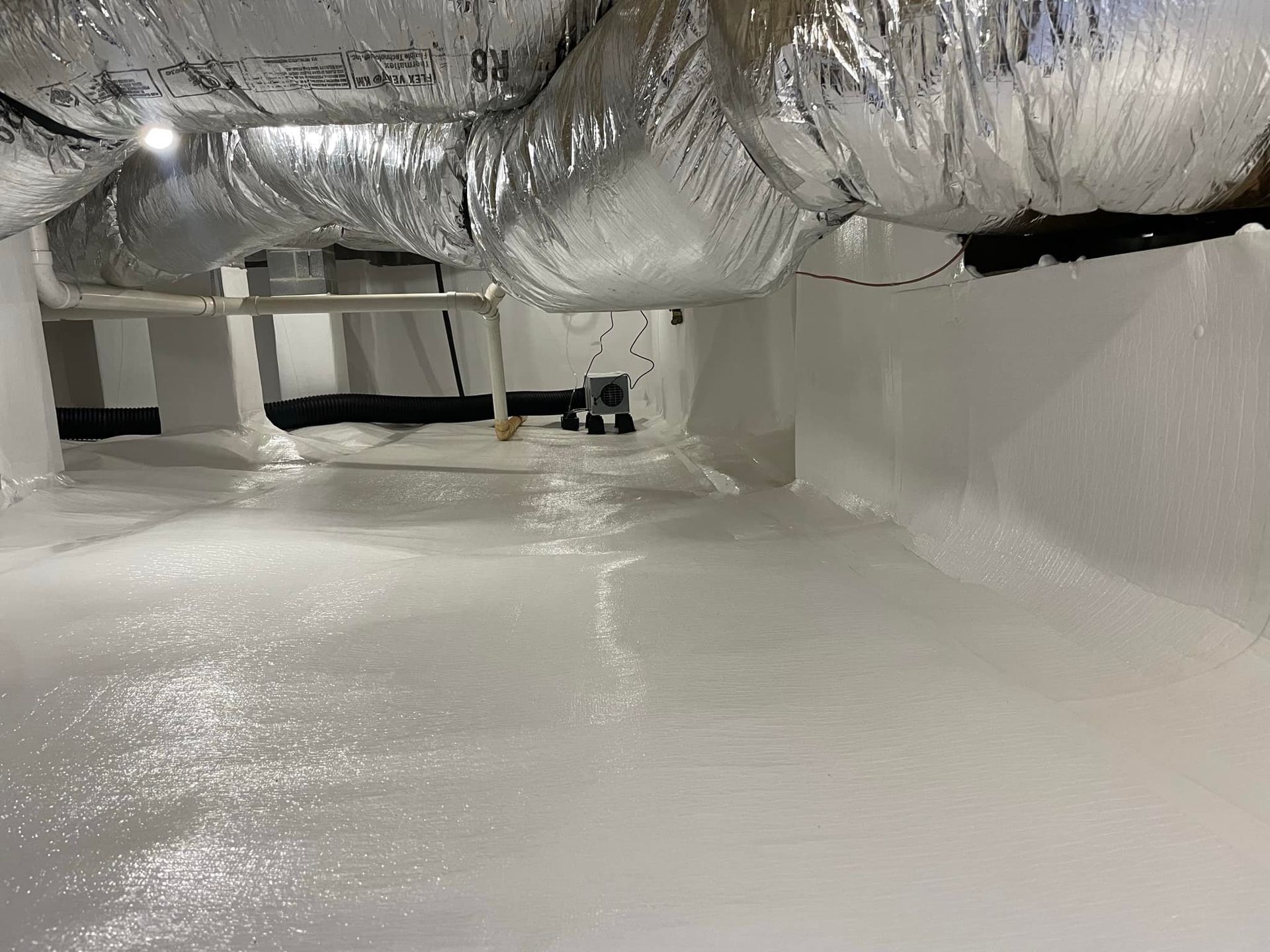 Interior view of a white-coated crawl space with silver HVAC ductwork overhead.