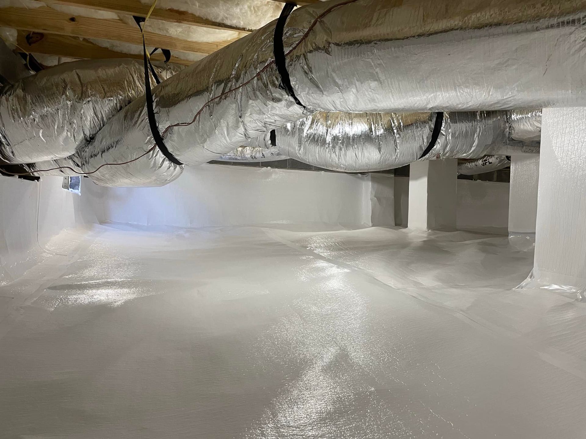 White-painted crawl space with reflective, silver ductwork overhead. Concrete pillars and floor are also painted.