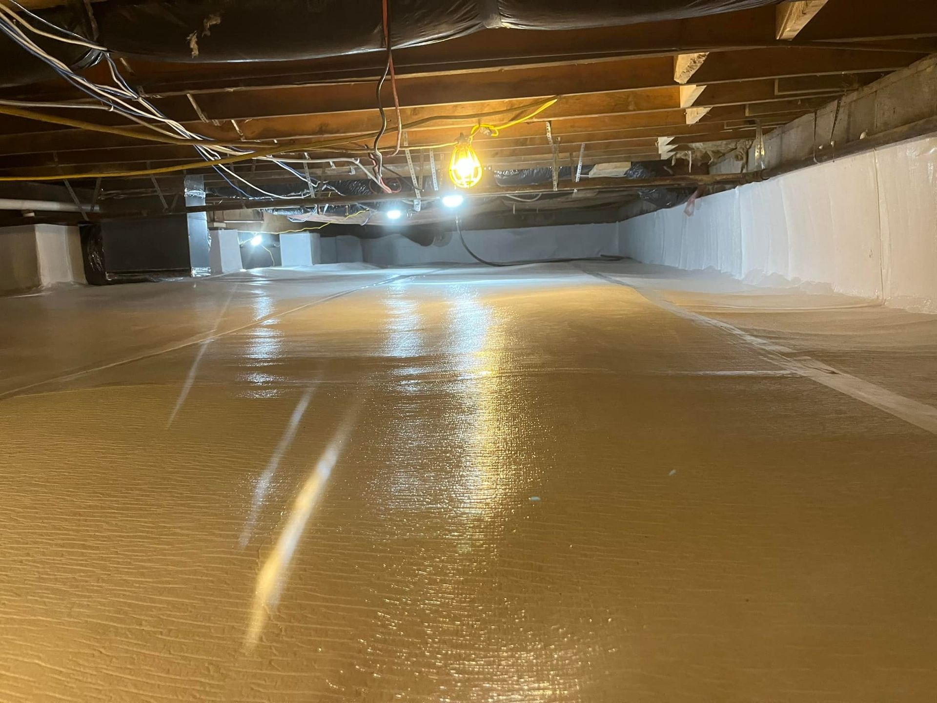 Interior of crawl space, with light-colored, sealed concrete floor and white walls. Lighting fixtures illuminate space.