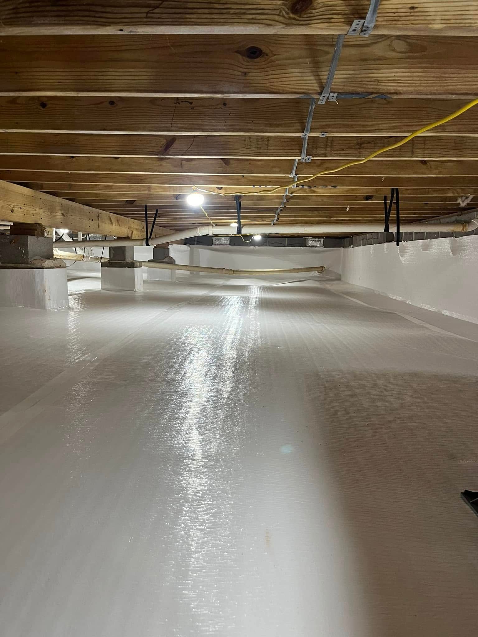 White crawlspace with insulation, wood beams, and support jacks.