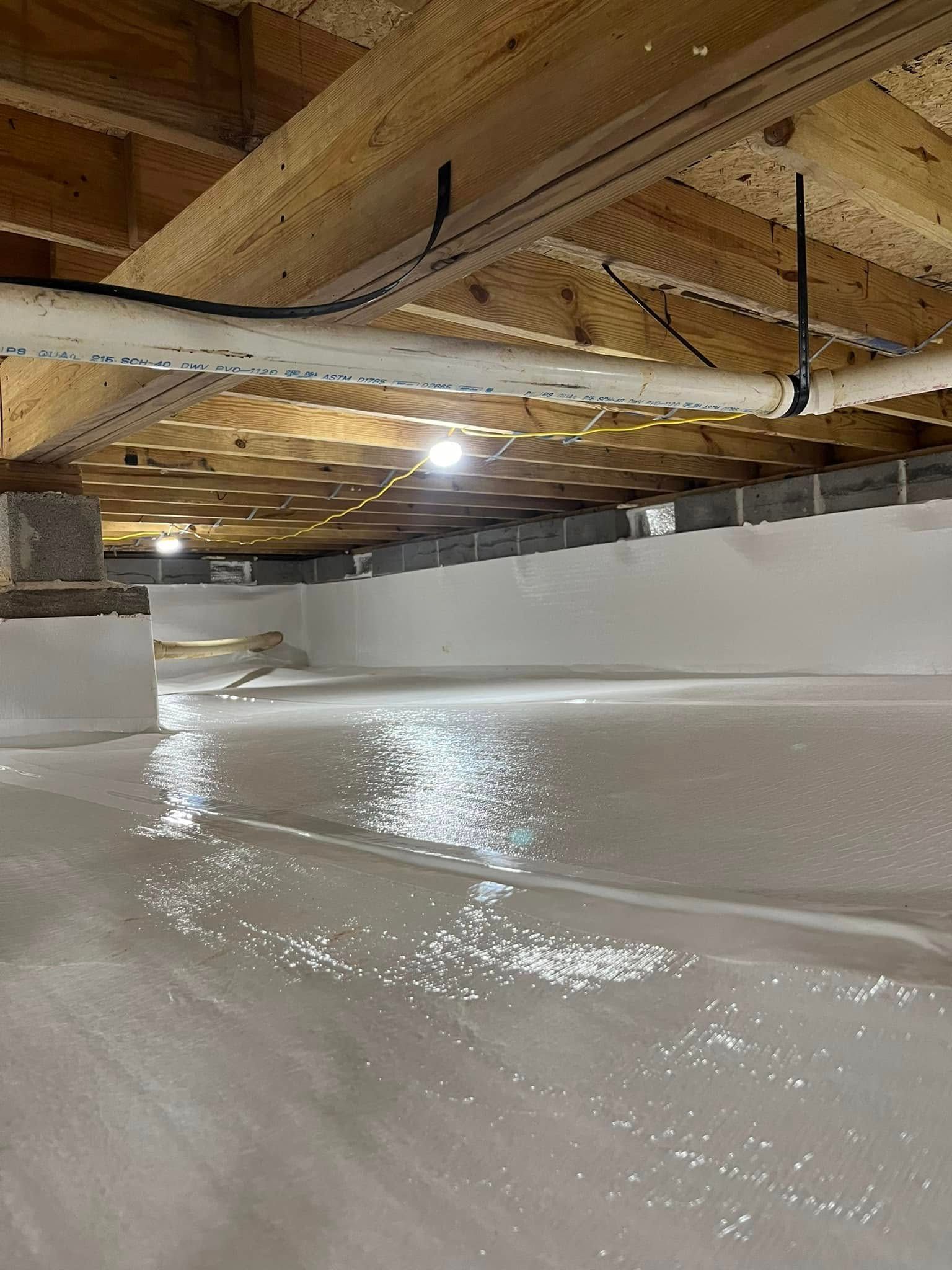 Bright white crawl space with insulation on walls, pipes overhead, and a light shining.