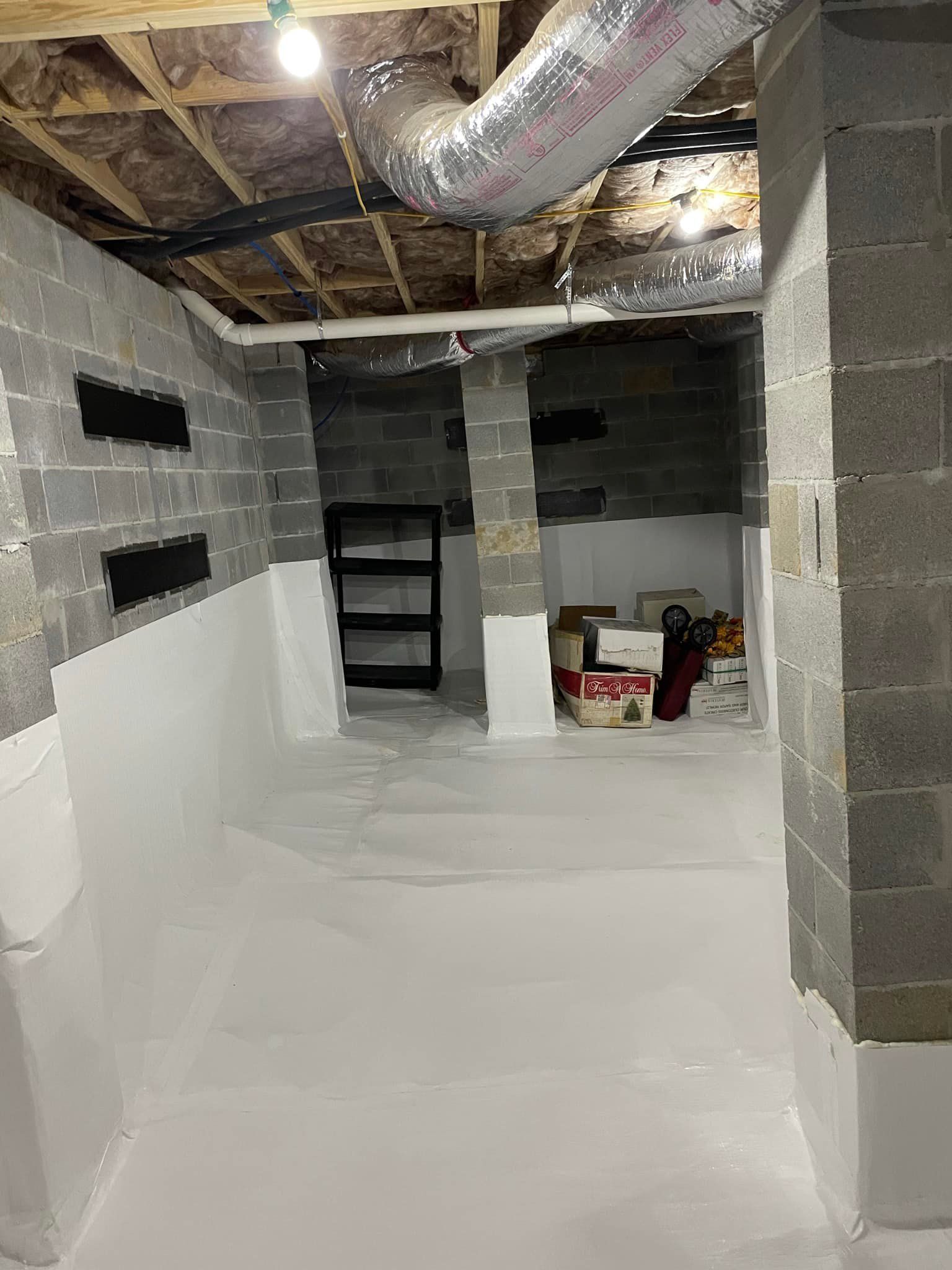 Basement interior with gray cinder block walls, white-painted lower walls, ductwork, and a black shelving unit.