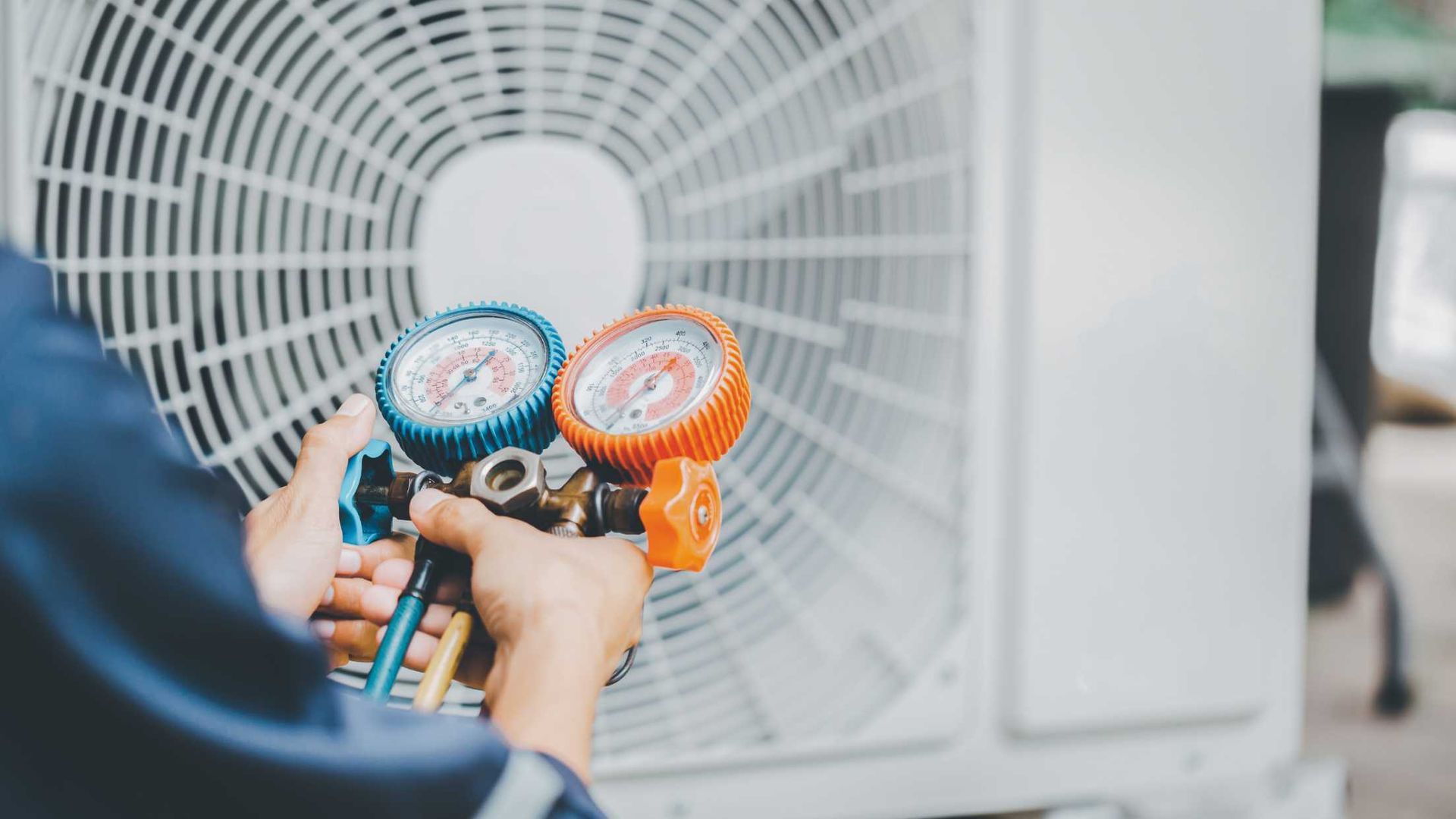 A man is working on an air conditioner with a pair of gauges.