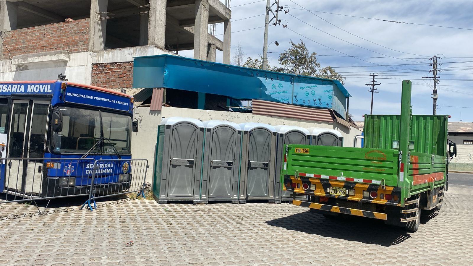 Un autobús azul, baños portátiles y un camión verde estacionados en una calle
