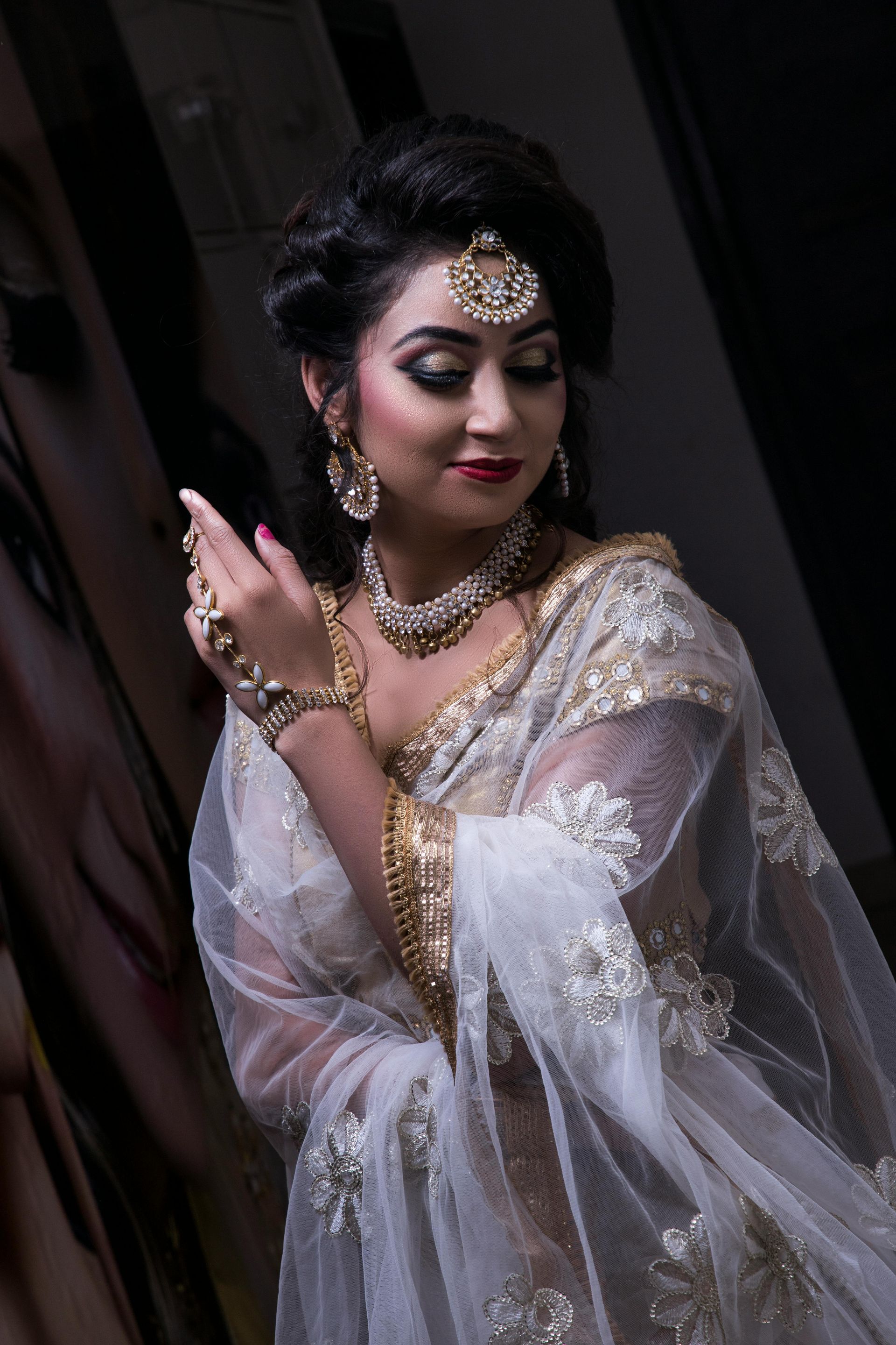 Woman in white and gold ethnic attire, wearing jewelry, with makeup and updo.