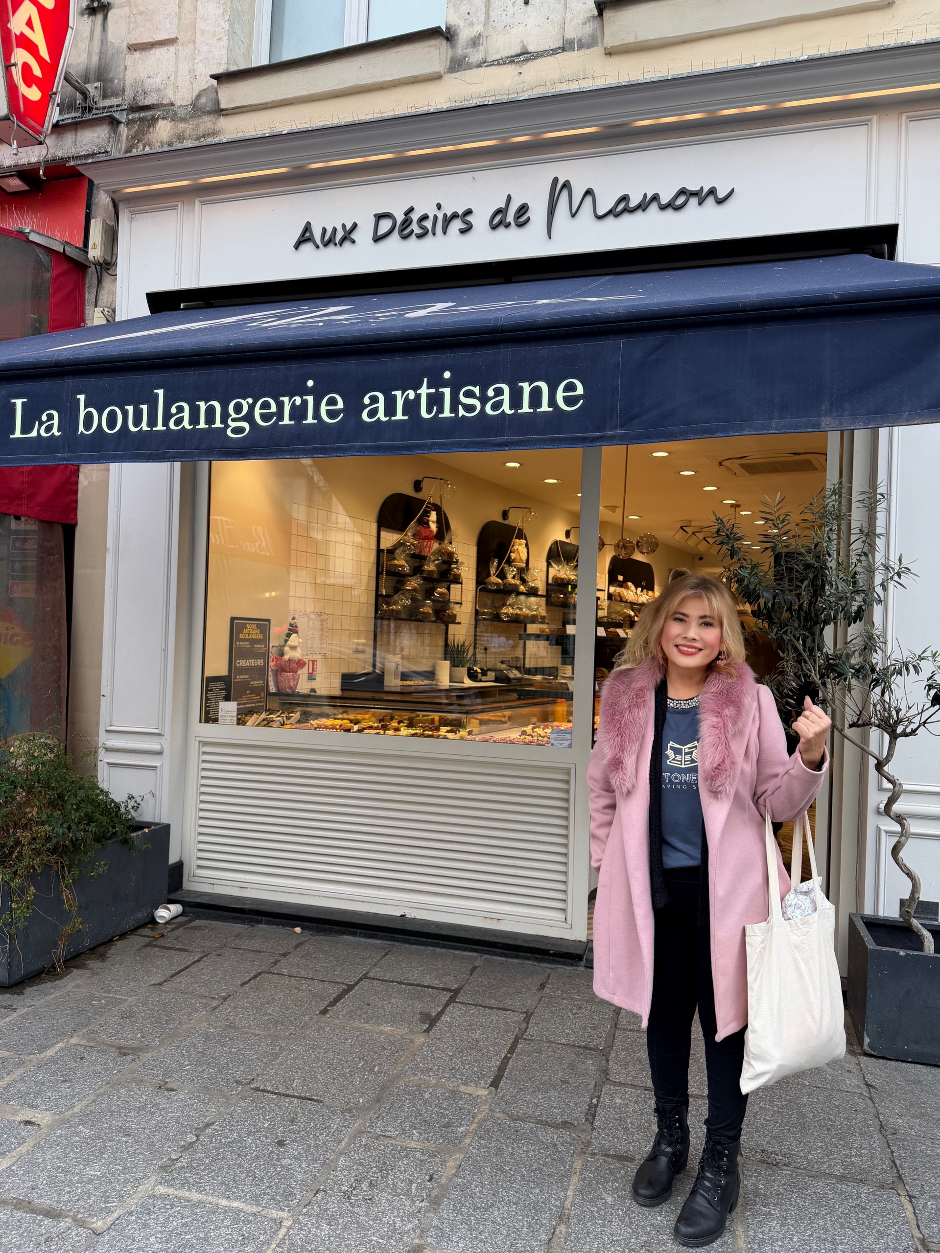 Woman in pink coat stands in front of a bakery called 