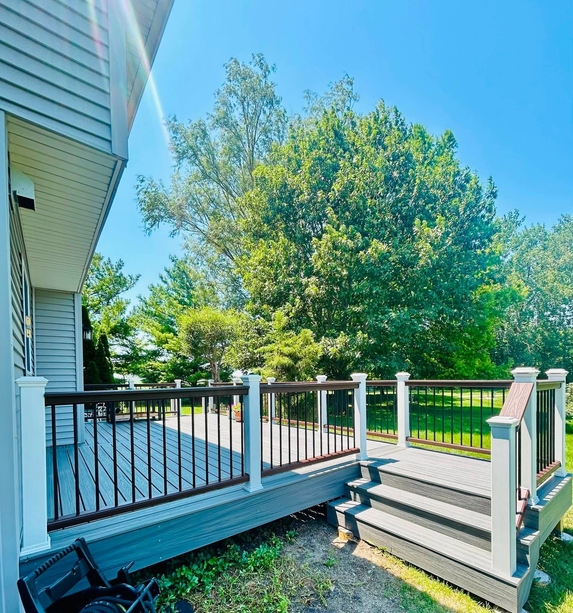 White house deck with railing and steps overlooking a sunny green backyard and large tree