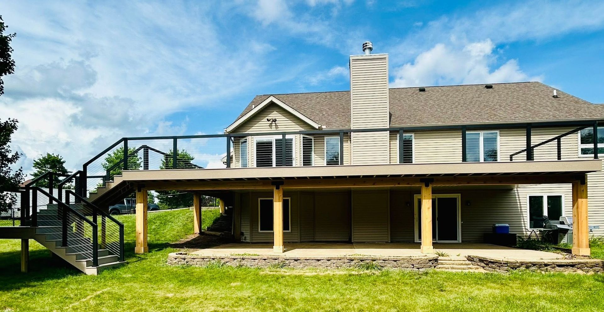 Backyard view of a two-story house with a covered patio, chimney, and staircase under a blue sky