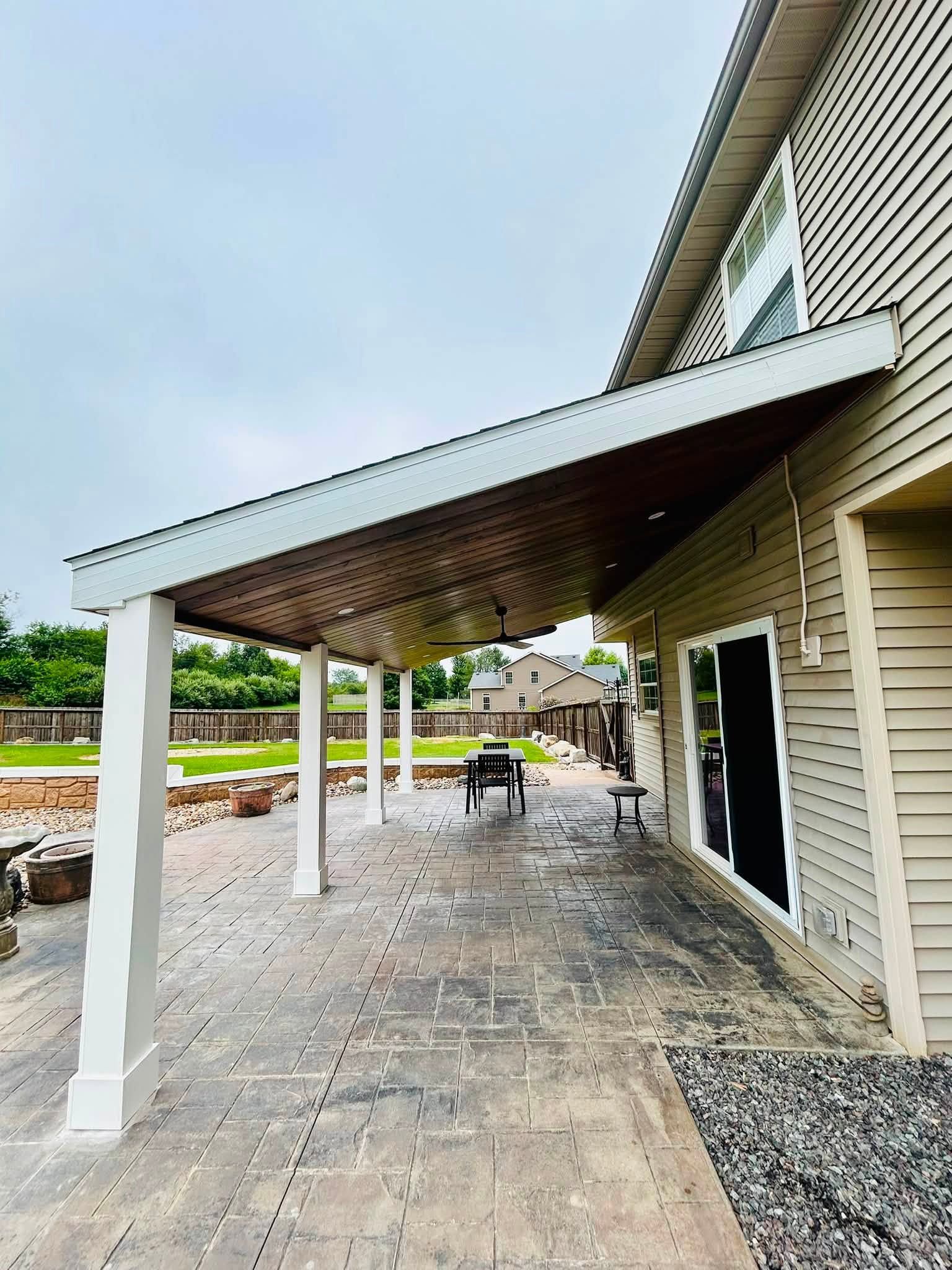 Covered patio beside a house with white columns, gravel ground, and a dining table under the roof.