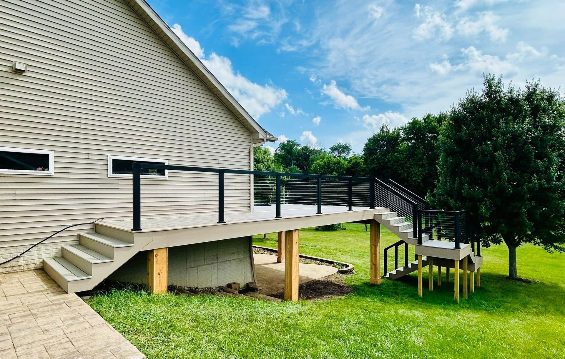 Wooden accessibility ramp with railings beside a house, leading to a grassy yard and trees.