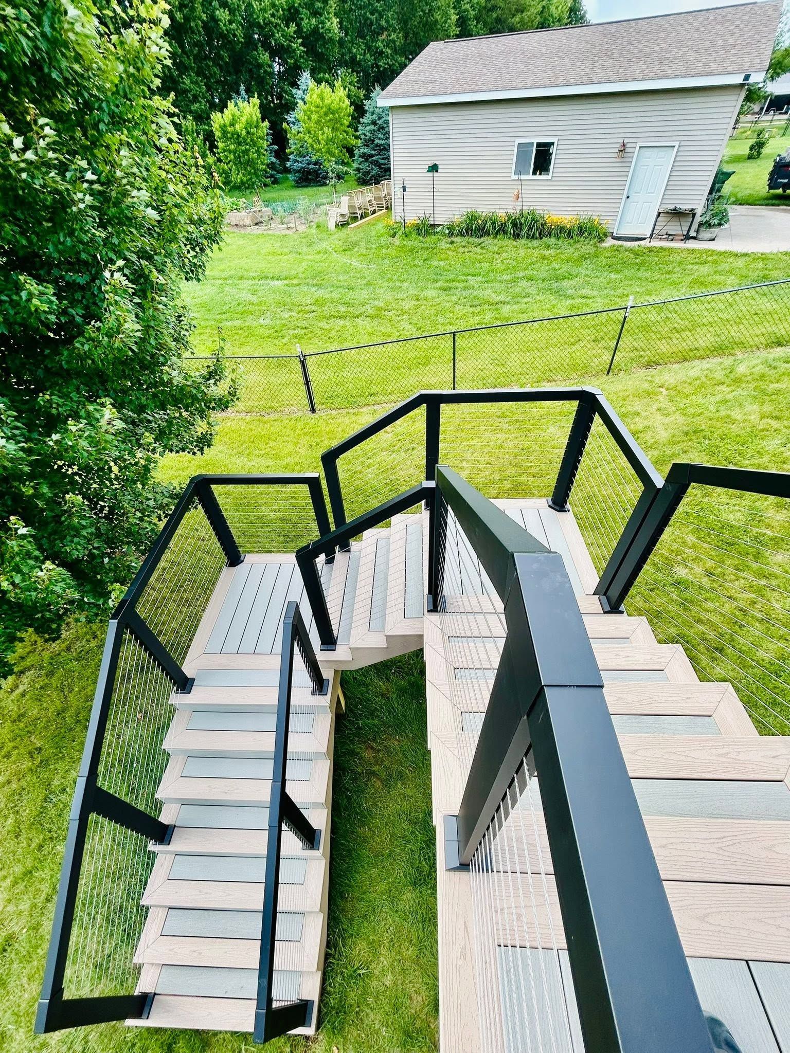 Outdoor stairwell with black railings descending beside a grassy yard and white house
