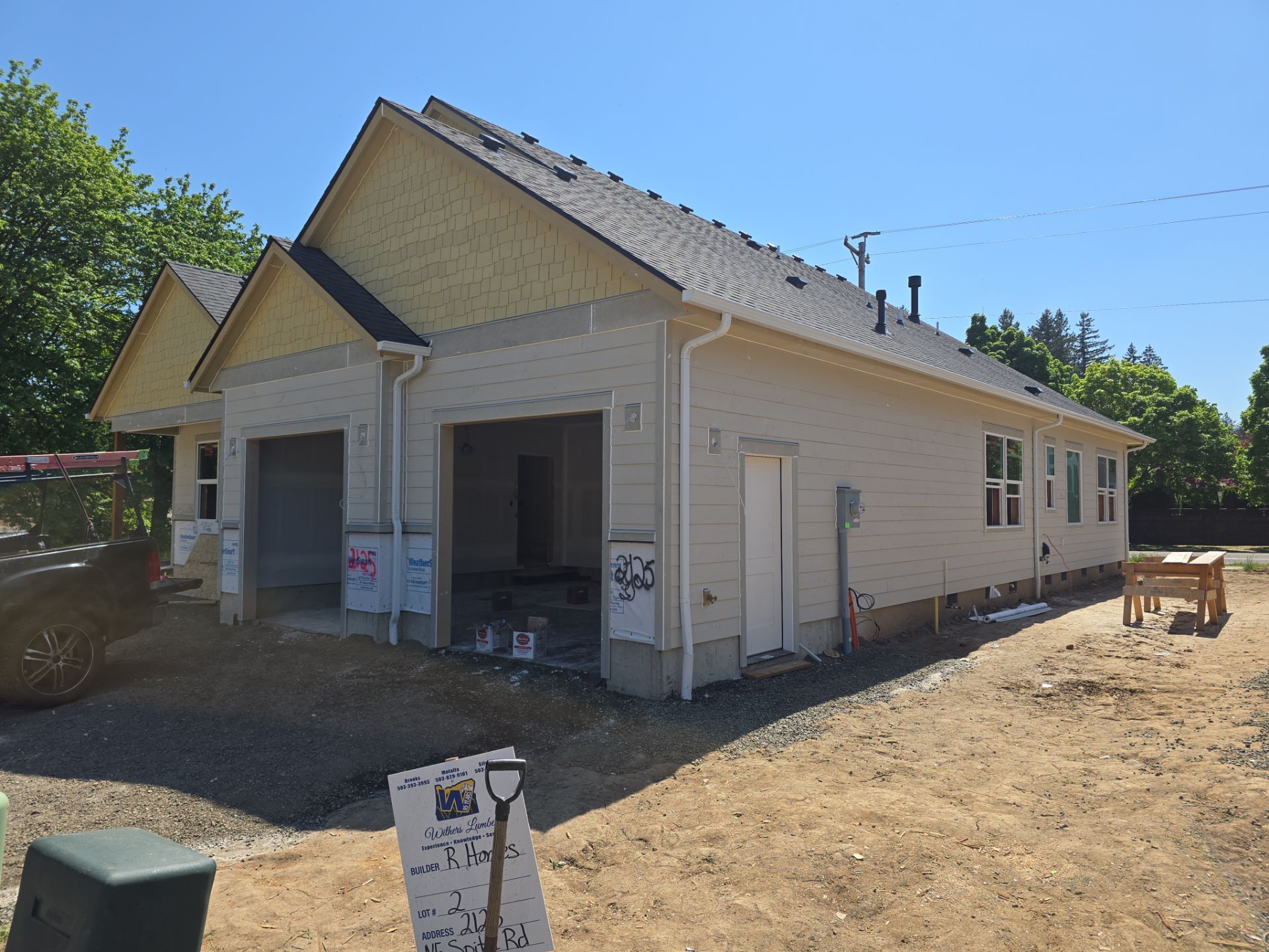 Single-story beige house under construction with open porch, dirt yard, and a sign in front