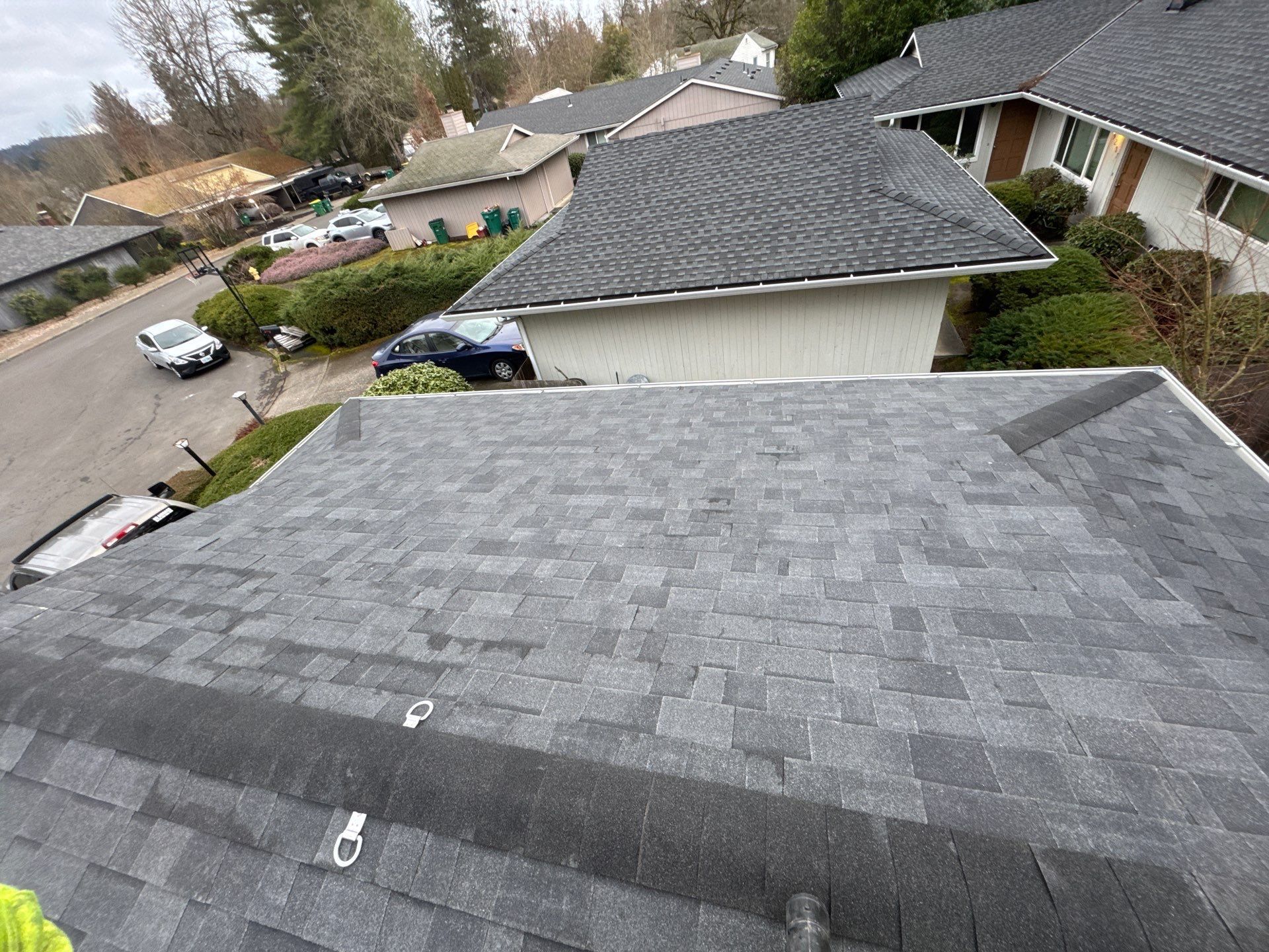 Overhead view of gray-shingled suburban rooftops and a parked car in a residential neighborhood