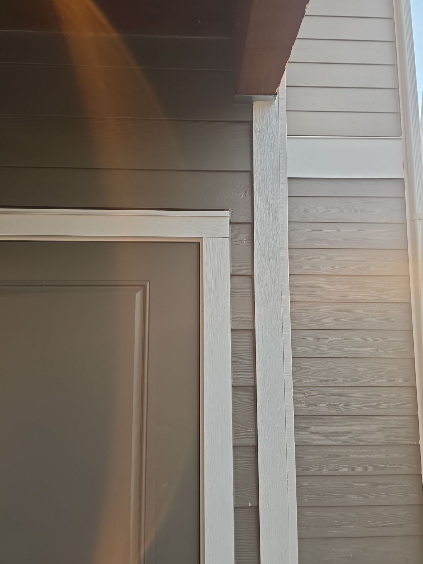 Close-up of a beige house exterior with white trim and horizontal siding at a roofline corner