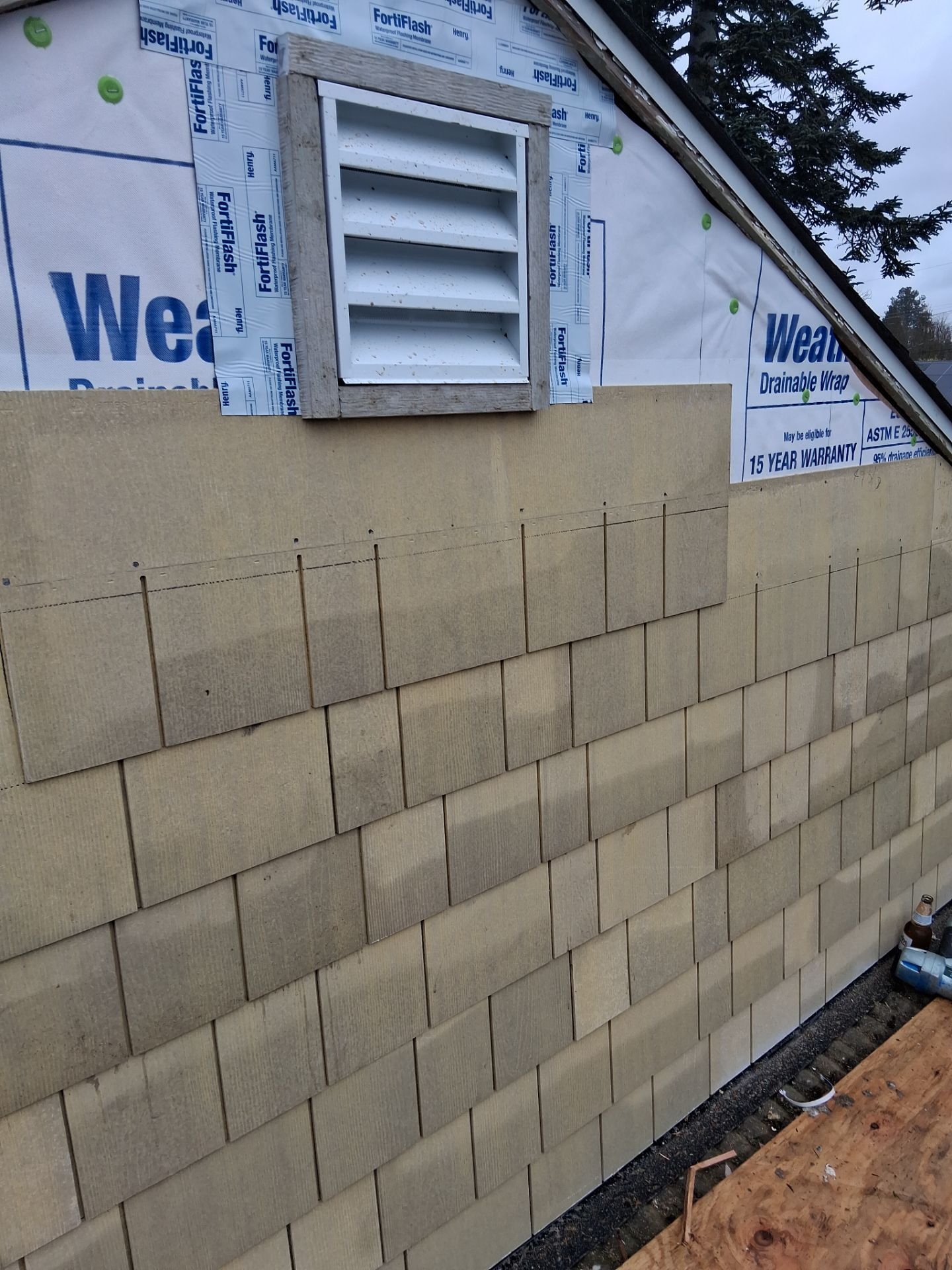 Partially finished exterior wall with beige cinder blocks, white vent, and house wrap near the roofline