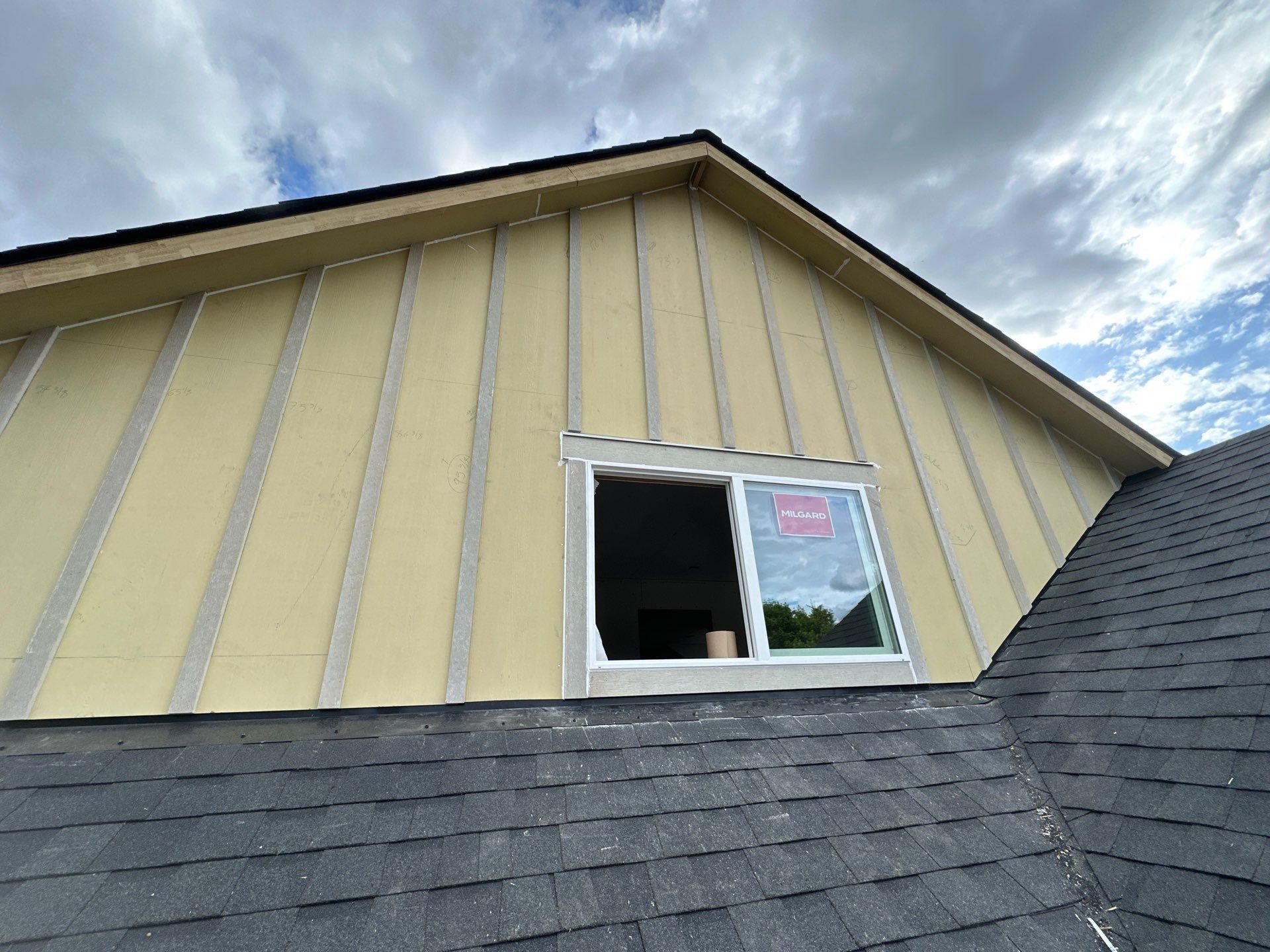 House exterior with yellow siding, gray roof, and an open window under a cloudy sky