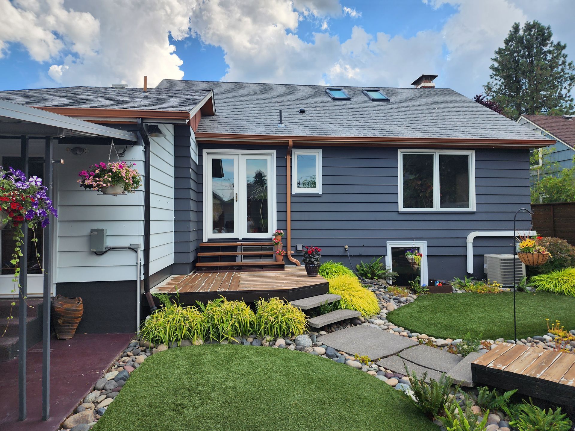 Single-story blue house with a front porch, flower beds, and a stone walkway under a cloudy sky