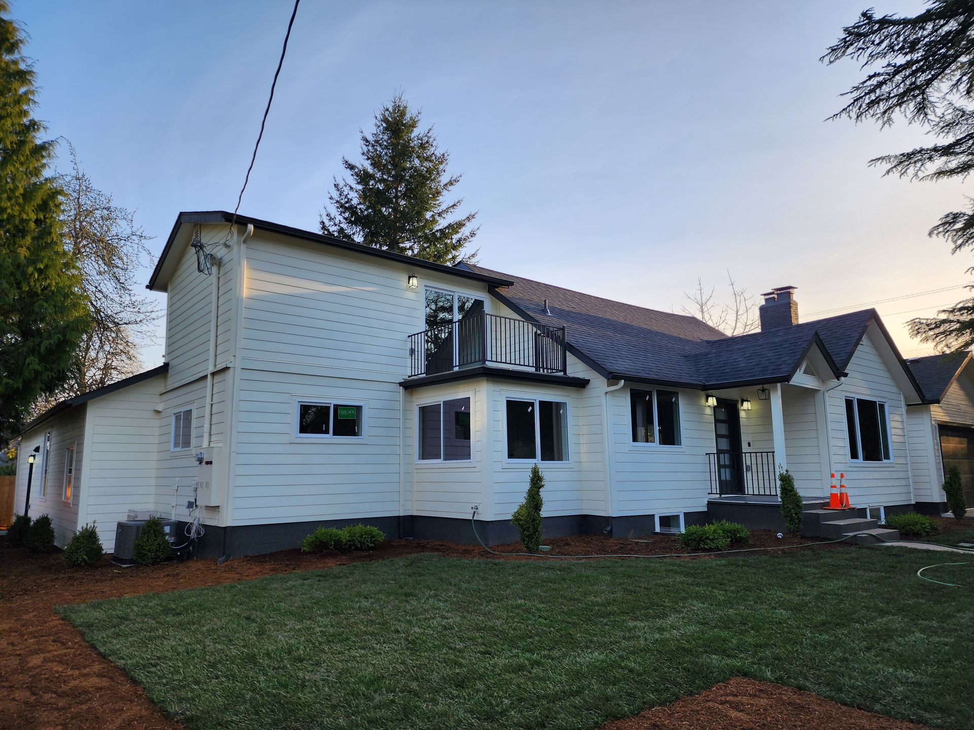 White suburban house with dark roof and white siding at dusk, viewed from the lawn