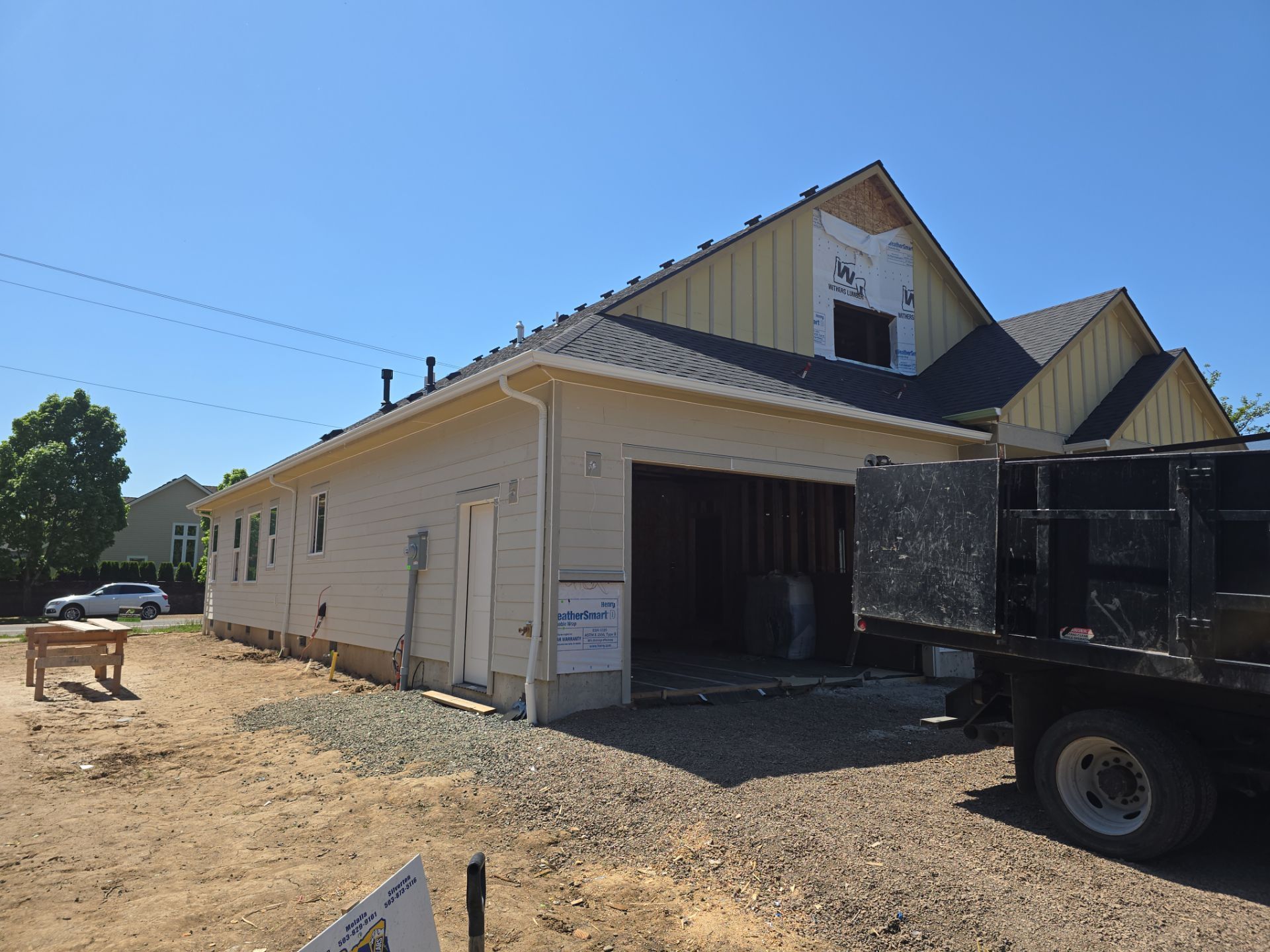 Rural beige building with open garage bay beside a parked black truck under a clear blue sky