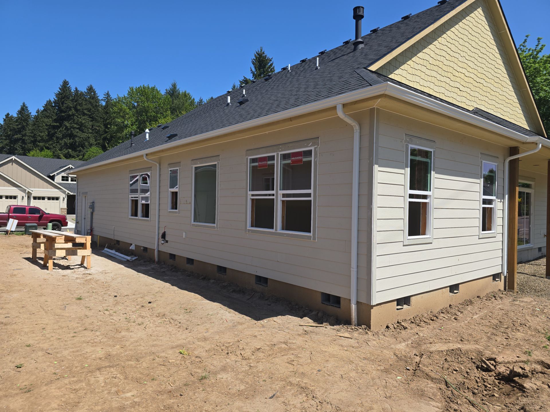 New beige house under construction with gravel yard and trees in the background