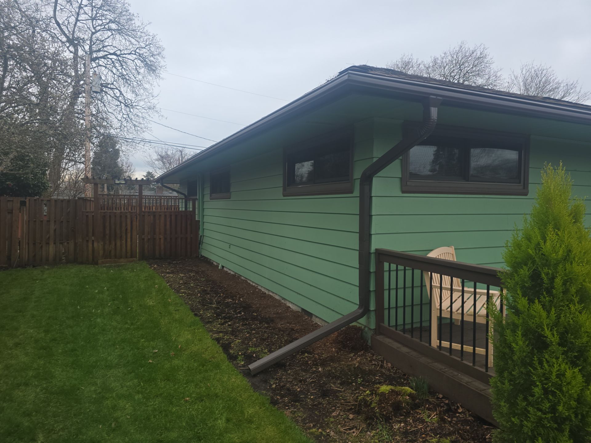 Green house exterior with sloped roof, fenced yard, and small deck in a wooded setting