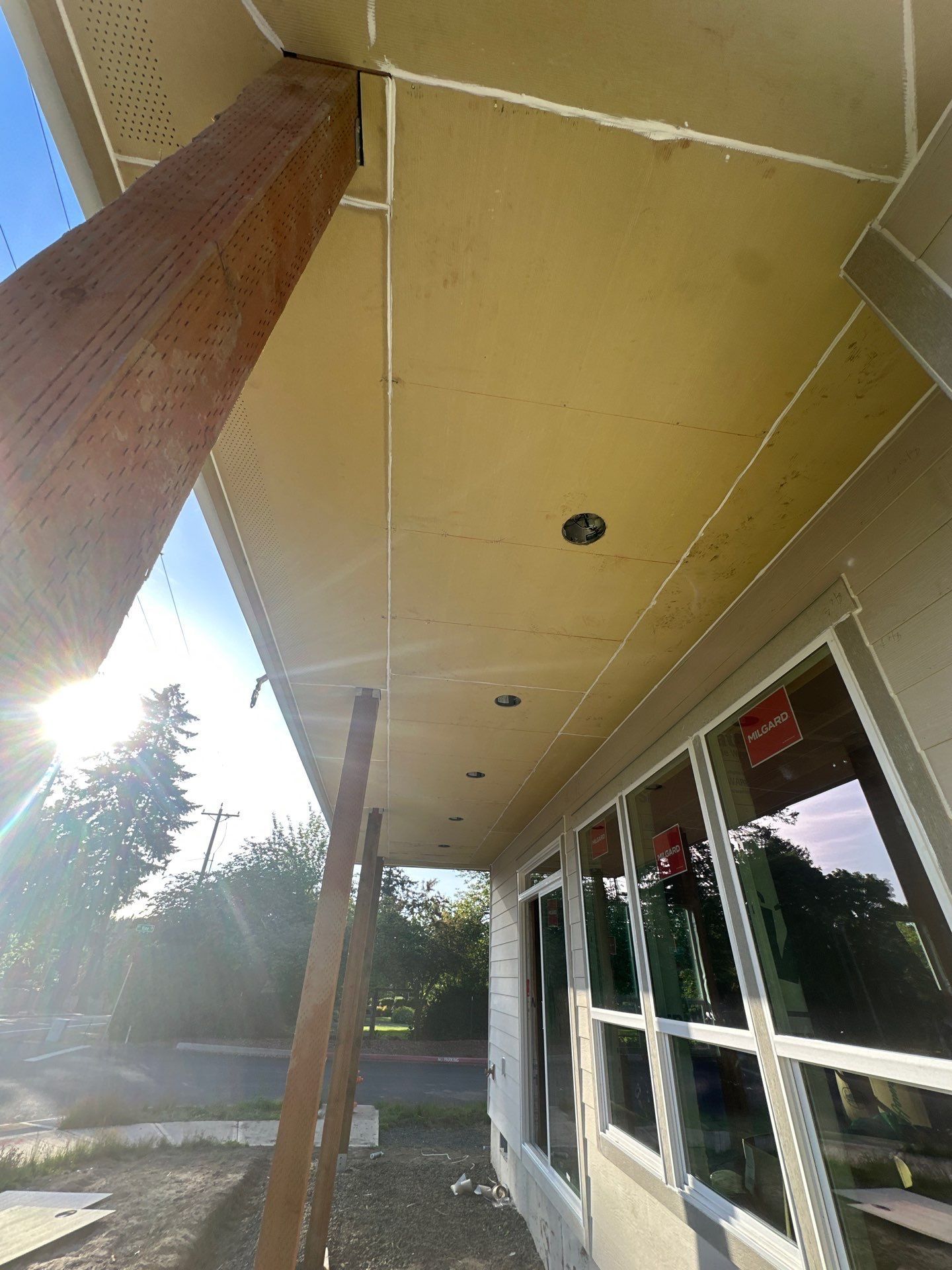 Covered building walkway with tan ceiling, wooden posts, and glass windows beside a parking area