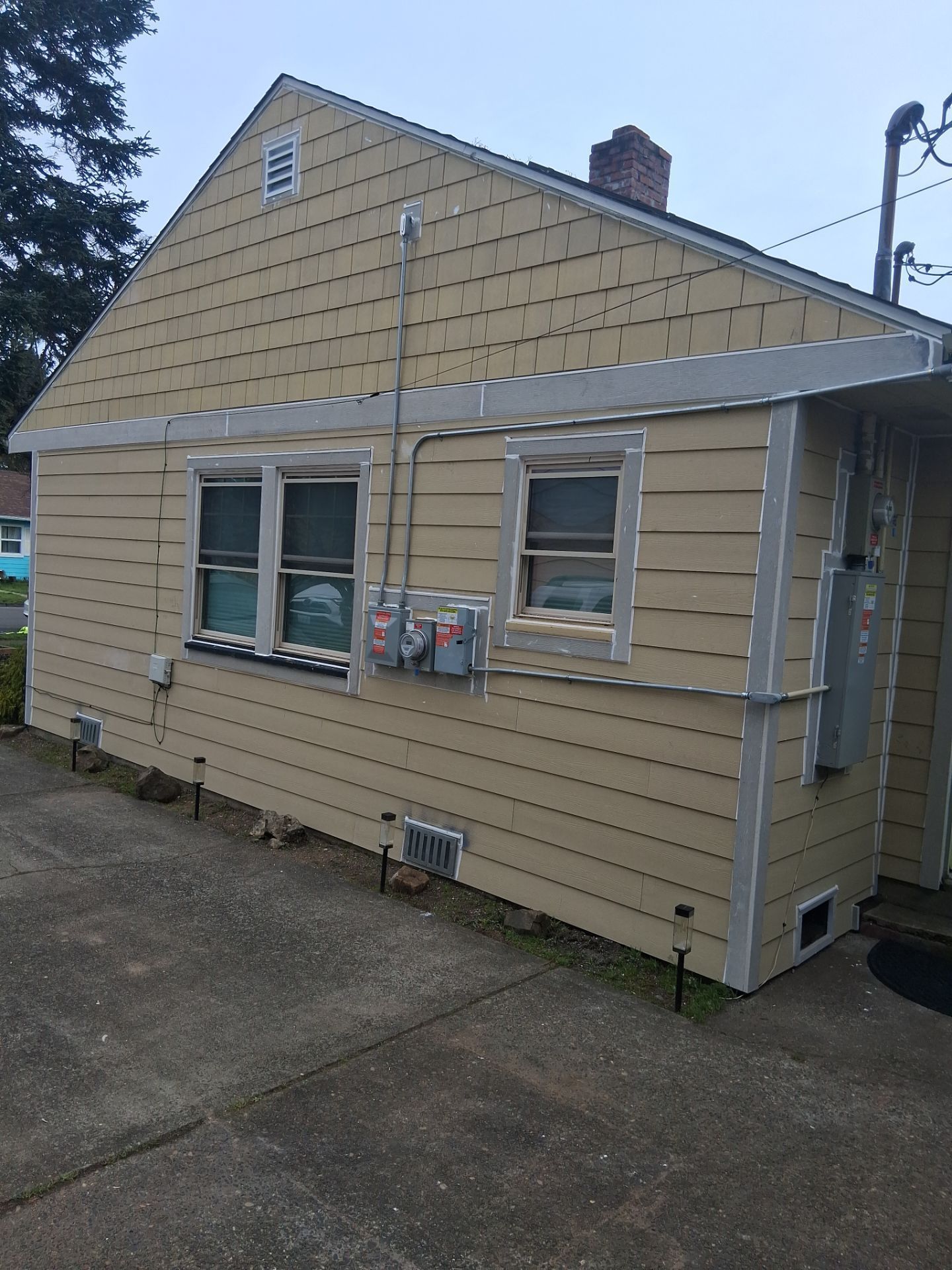 Beige house with vinyl siding and two windows, viewed from the side on a paved driveway.