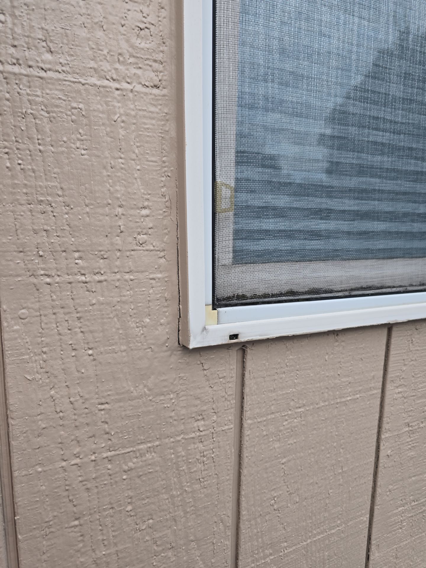 Close-up of a beige house wall with a white-framed window and screen.