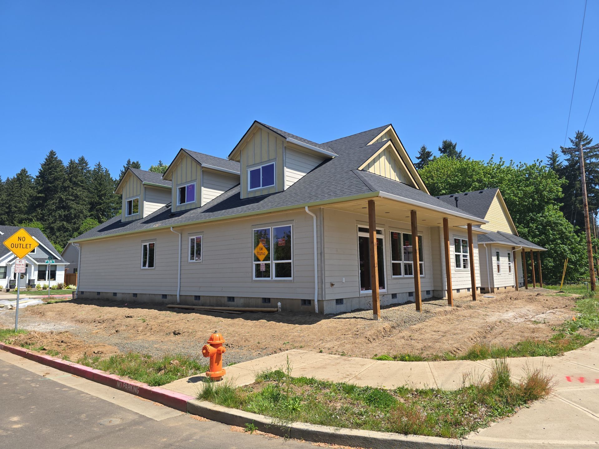 New house under construction on a sunny corner lot, with beige siding and a red fire hydrant in front.